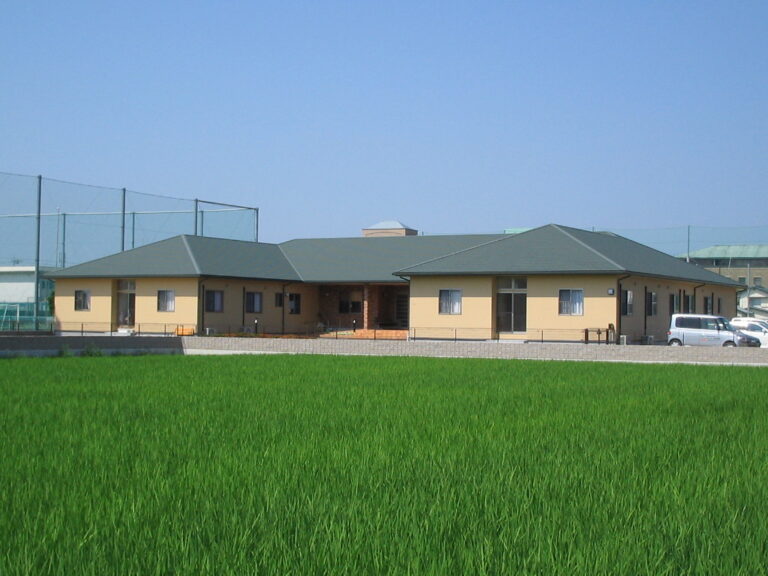 田園地帯に建つ平屋建ての介護施設。緑屋根と黄色い外壁が特徴の建物。